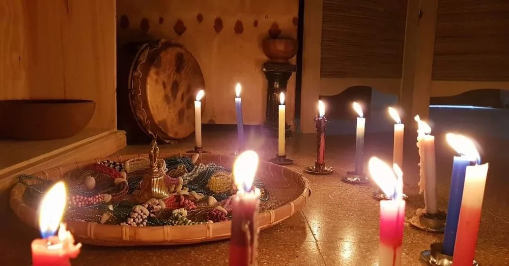 Altar ritual con velas encendidas, collares ceremoniales y un tambor tradicional al fondo