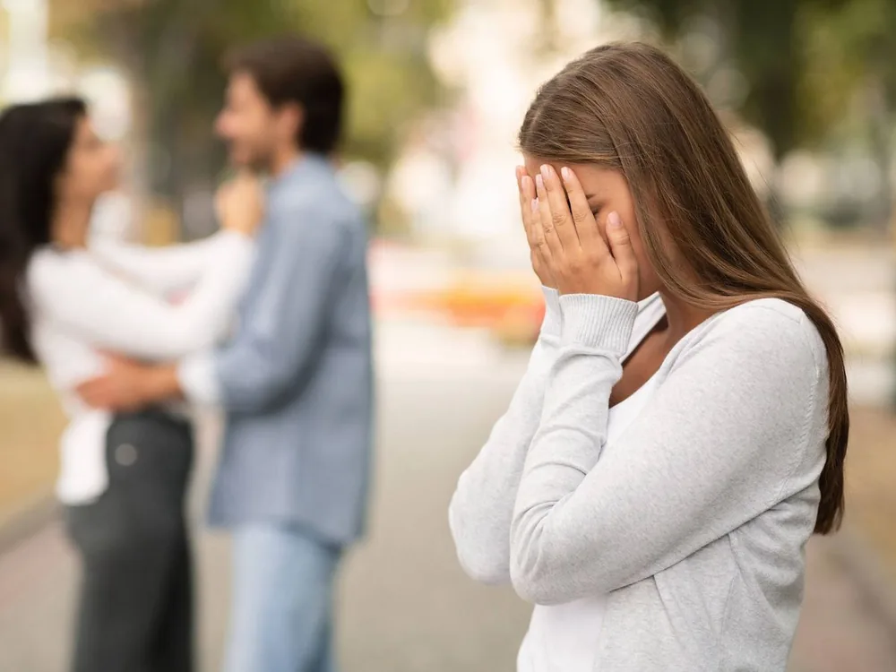 Mujer procesando en soledad la distancia de una relación, con una pareja desenfocada al fondo