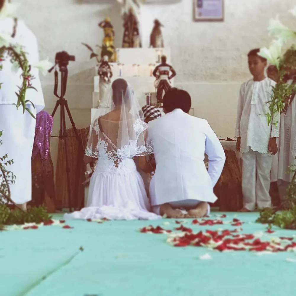 Pareja arrodillada frente a un altar durante una ceremonia de unión, rodeada de pétalos de rosa